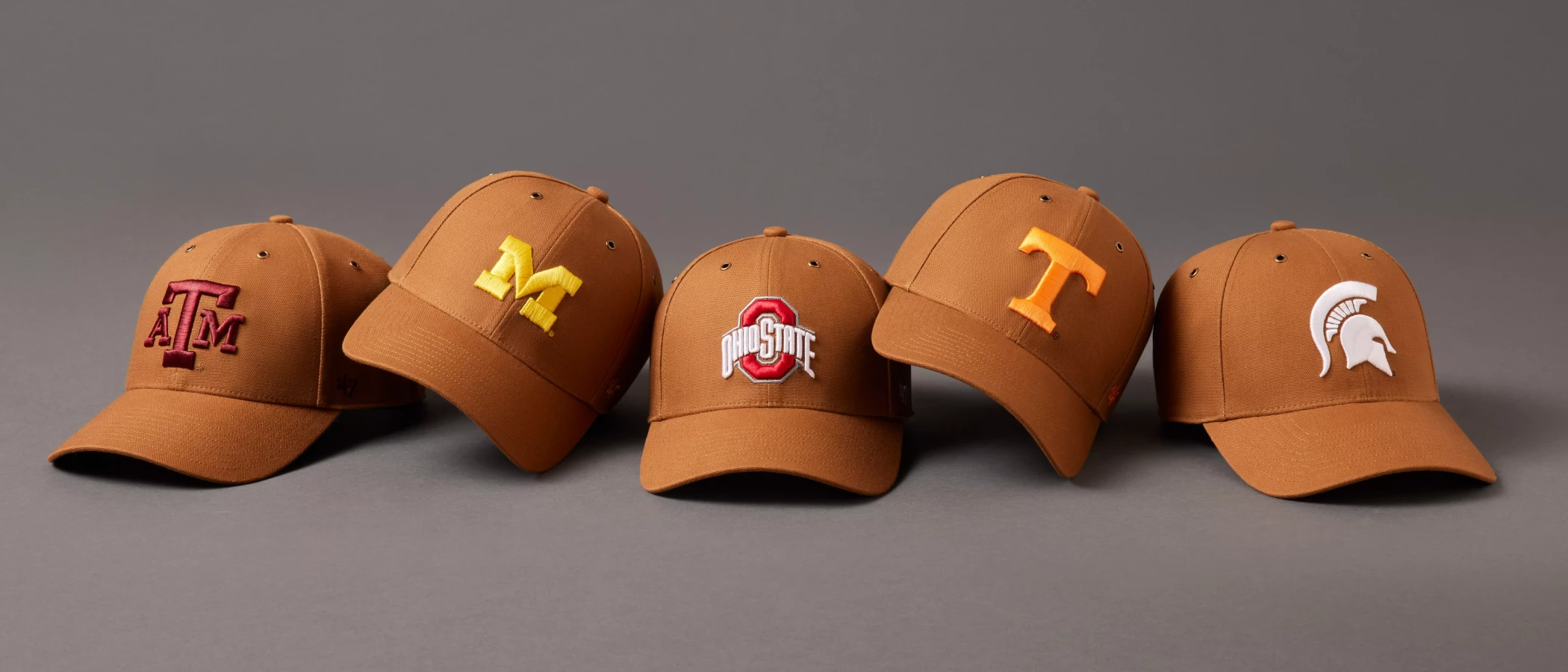 5 '47 x Carhartt hats on a dark gray background. from these schools in order from left to right: Texas A&M, Michigan, Ohio State, Tennessee, Michigan State